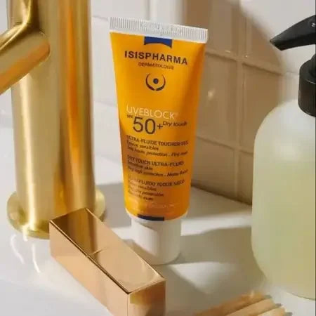 Sunscreen tube labeled 'Isispharma' on a bathroom shelf with a gold faucet